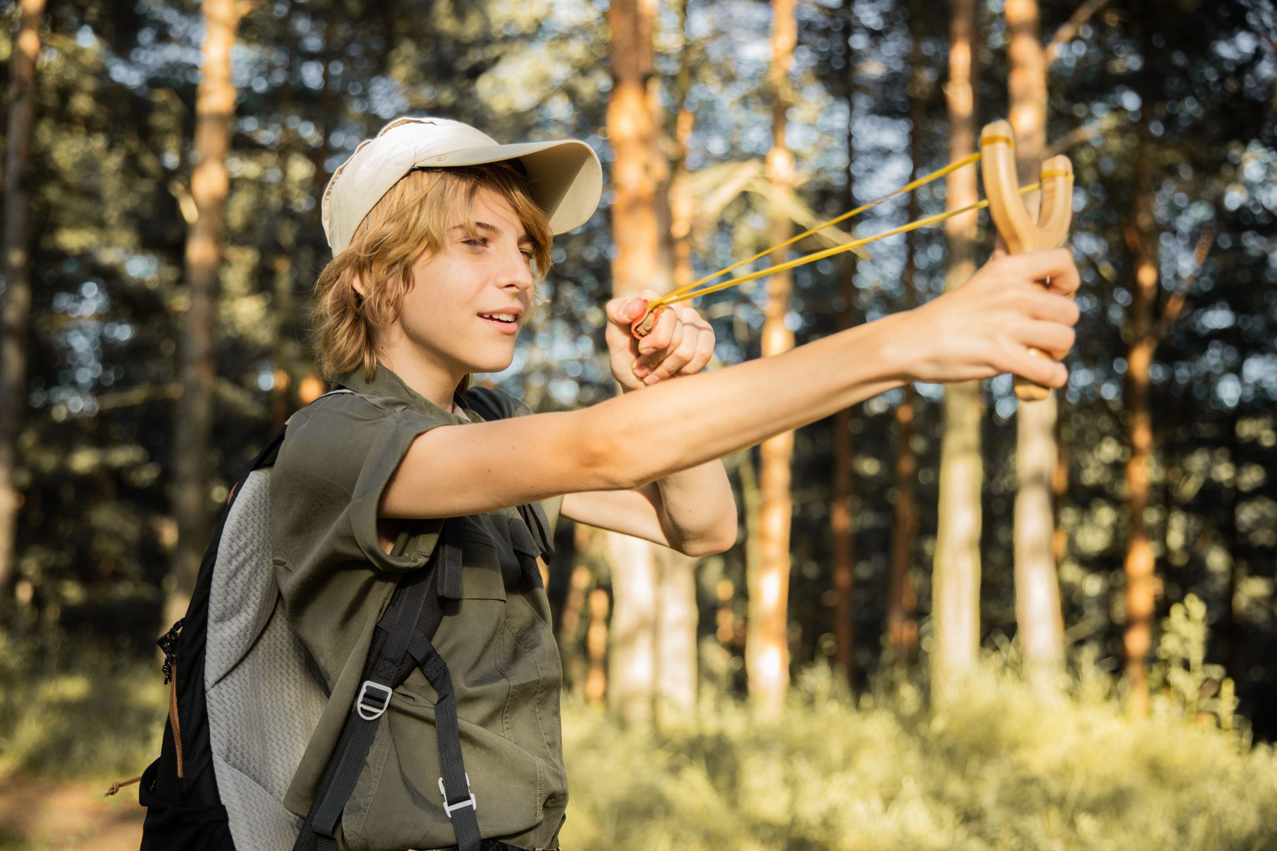 A teenager enjoys an outdoor adventure playing in the forest with a slingshot.
